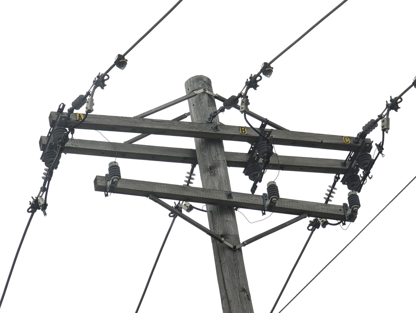 Photograph looking up at the top of a wooden utility pole carrying a three-phase Ameren Missouri distribution line, with crossarms, insulators and fused cutouts against a white sky.
