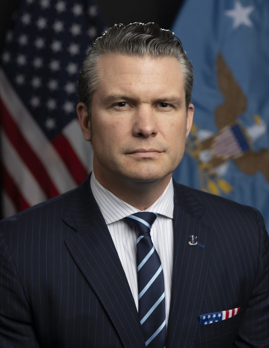Official portrait photograph of Secretary of Defense Pete Hegseth in a dark pinstriped suit in front of the U.S. flag and the Department of Defense flag, January 2025.